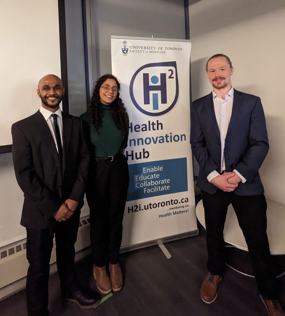 The three pitch competition winners stand altogether, smiling with hands clasped, in front of the Health Innovation Hub banner.